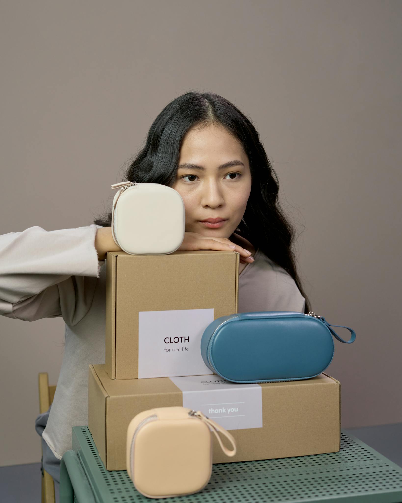 Stylish woman in studio with luxury handbags stacked on cardboard boxes, neutral background.
